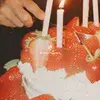 Close-up of a strawberry-topped cake with lit candles and a hand holding a knife, ready to cut. Text reads "Bryllup i Postsalen".